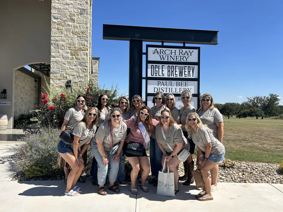 A bachelorette group in matching heart sunglasses posing under the Arch Ray Winery sign.