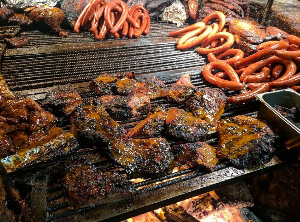 Sausage links and ribs cooking over open coals on the pit at The Salt Lick BBQ.