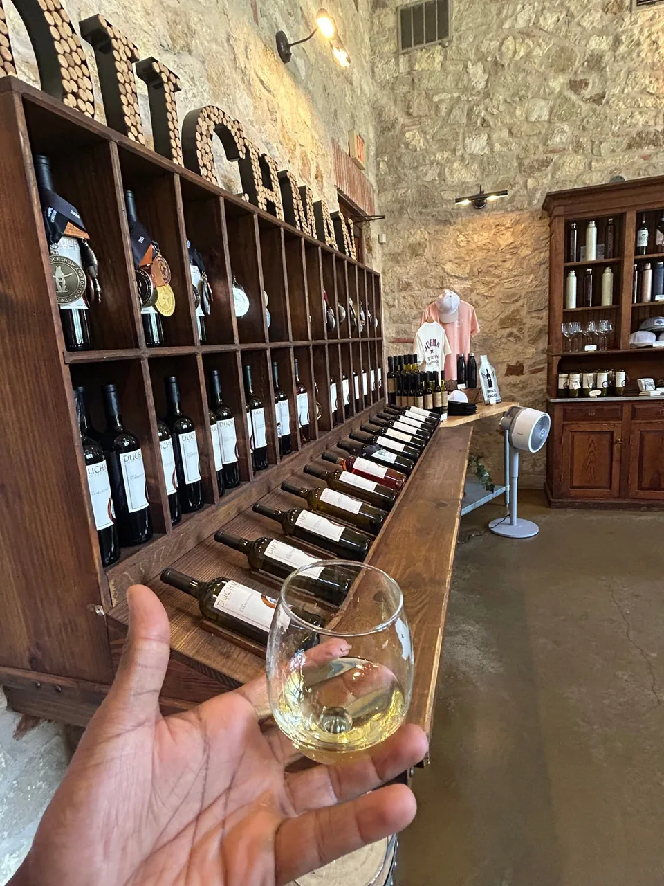 A glass of white wine held up in a stone tasting room.