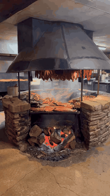The open pit at The Salt Lick BBQ — sausage links hanging over racks of ribs and brisket, wood fire glowing below.