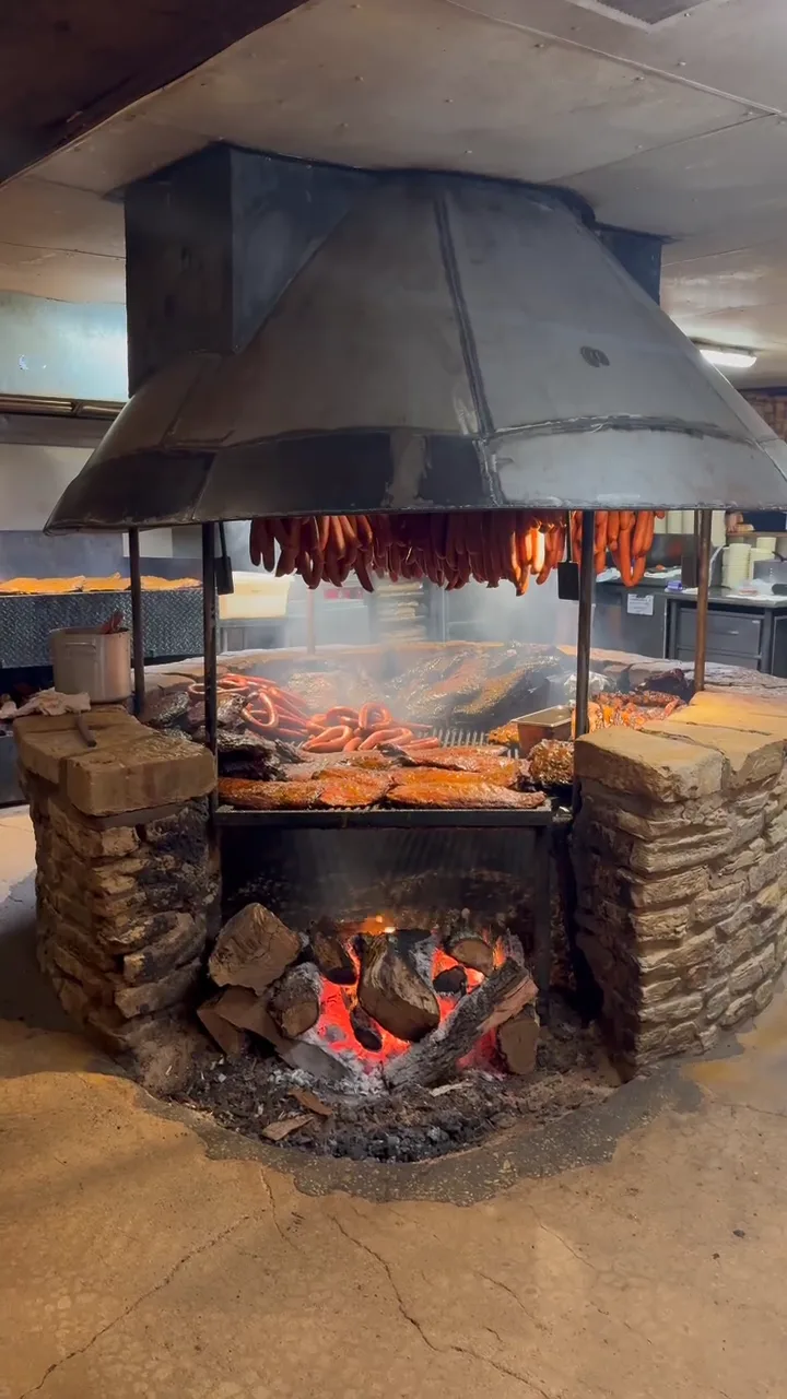 The open pit at The Salt Lick BBQ — sausage links hanging over racks of ribs and brisket, wood fire glowing below.